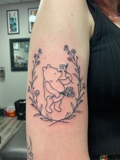 A line work tattoo of a traditional Winnie the pooh as drawn by E. H. Shepard holding a bundle of violets and surrounded by a wreath of peonies positioned on the left bicep. Classic Pooh And Piglet, American Traditional Winnie The Pooh Tattoo, Hundred Acre Wood Tattoo, Vintage Pooh Tattoo, Subtle Winnie The Pooh Tattoo, Tigger And Pooh Tattoo, Vintage Winnie The Pooh Tattoo, Winnie The Pooh Outline Tattoo, Classic Pooh Tattoo