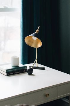 a table with a lamp and books on it in front of a window, next to a pair of curtains