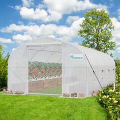 a green house with flowers growing in the ground and trees behind it on a sunny day