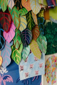 colorful paper leaves are hanging on the wall in front of a blue tablecloth with white and green designs