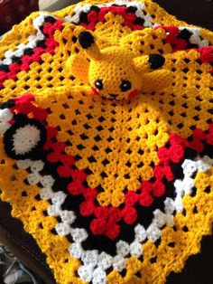 a crocheted teddy bear is on top of a yellow and black blanket with red, white, and black circles