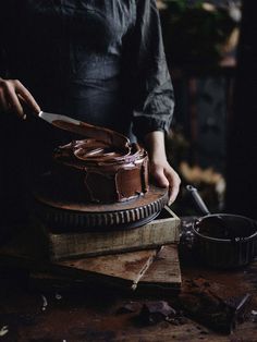 a person cutting a chocolate cake on top of a wooden board with a knife in it