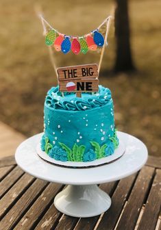 a blue cake sitting on top of a wooden table next to a sign that says the big one