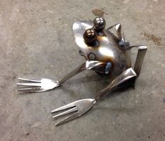 a metal frog sitting on the ground with two forks sticking out of it's back