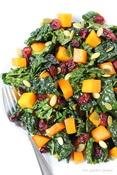 a white plate topped with spinach, cranberries and pumpkins next to a fork