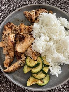 a plate with chicken, rice and zucchini on it is sitting on the floor