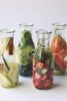 four glass vases filled with different types of vegetables