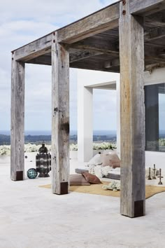 an outdoor living area with couches, pillows and wooden pillars in front of the house