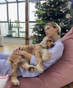 a woman sitting on a couch with two dogs in her lap and christmas tree in the background