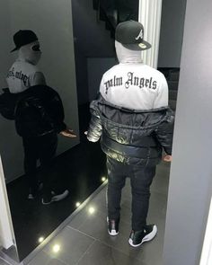 a man standing in front of a mirror wearing a black and white jacket with the words mini angels on it