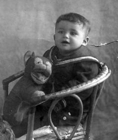 an old black and white photo of a young boy sitting in a chair holding a teddy bear