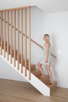 a woman is walking up the stairs in a house with white walls and wood flooring