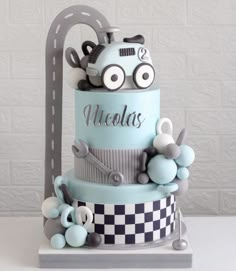 a three tiered cake with cars on top and checkerboard design is displayed in front of a white brick wall