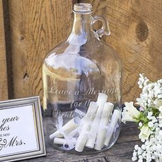 a glass bottle with some candles in it next to a sign and flowers on a table