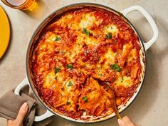 a person holding a spoon in a large pan of food with sauce and cheese on it