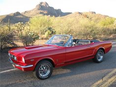 an old red mustang convertible parked on the side of the road