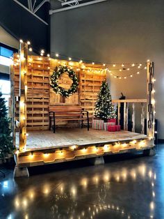 a stage set up with christmas lights and wreath on the top, surrounded by small trees