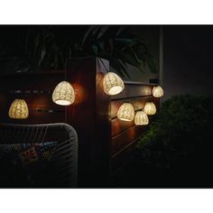 several lights are lit up on the side of a wooden structure at night, with plants in the background