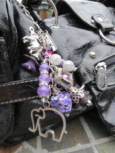 a black purse with purple and silver charms hanging from it's side on a stone floor