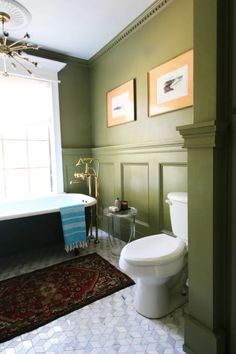 a white toilet sitting next to a bath tub in a bathroom under a painting on the wall