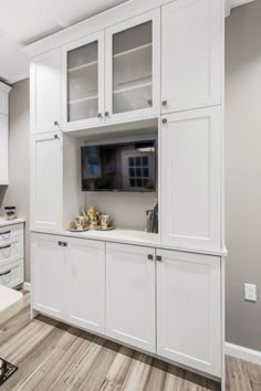 a kitchen with white cabinetry and wood flooring in the center, along with a flat screen tv mounted to the wall