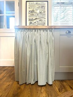 a kitchen counter with a curtain over it in front of a window and a painting on the wall