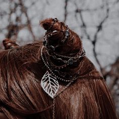 a woman with long brown hair wearing a chain around her neck and a leaf shaped brooch