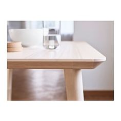 a wooden table with a white bowl on top of it and a glass in the background