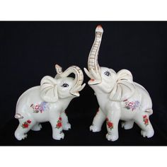 two white ceramic elephants standing next to each other on a black background with red and blue flowers