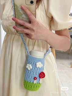 a woman holding a cell phone and wearing a crocheted purse with mushrooms on it