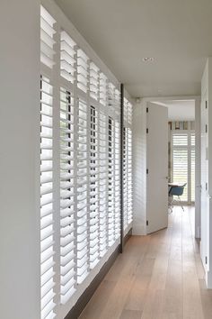 an empty hallway with wooden floors and white shutters on the walls, leading to a computer desk