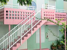 a pink and green building with stairs leading up to the second floor, surrounded by plants