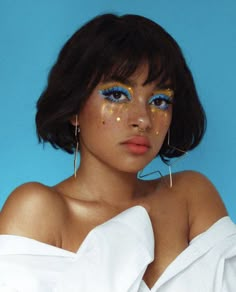 a woman with blue eyes and gold glitter on her face, wearing large hoop earrings