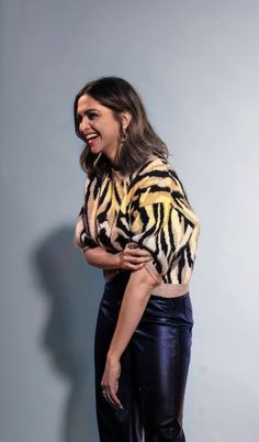 a woman standing in front of a gray wall wearing black pants and a tiger print sweater