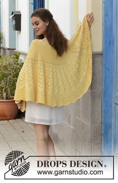 a woman wearing a yellow shawl standing next to a blue door and potted plant