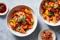 three bowls filled with pasta and vegetables on top of a blue countertop next to sauces