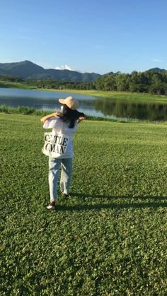 a woman standing on top of a lush green field next to a body of water