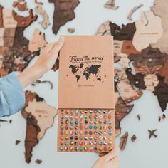 someone holding up a travel the world book in front of a map with pins on it