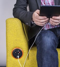 a man sitting on a yellow couch holding an electronic device and plugged into the cord