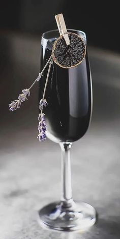 a wine glass filled with black liquid and lavender sprigs