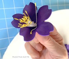 a hand holding a purple flower on top of a white countertop next to a blue tiled wall