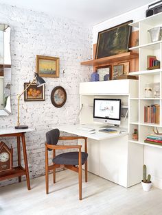 a desk with a computer on top of it in front of a white brick wall