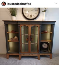 a large clock mounted to the side of a wall next to a wooden cabinet with glass doors