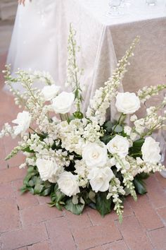 a bouquet of white flowers sitting on top of a brick floor next to a table