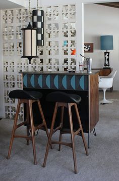 two bar stools sitting in front of a counter with lights hanging from the ceiling