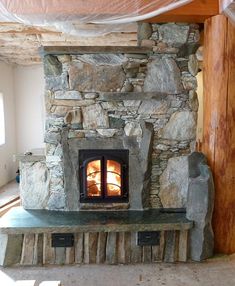 a stone fireplace in the middle of a room with wood and rocks on it's sides