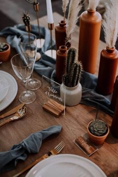 a wooden table topped with lots of white plates and silverware next to tall brown vases