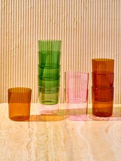 four different colored glasses sitting on top of a white table next to a striped wall