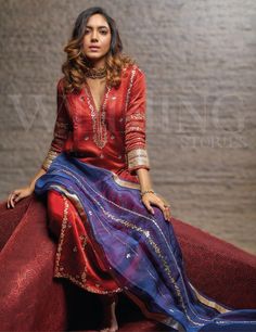 a woman sitting on top of a red couch wearing a blue and red dress with gold accents