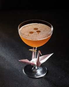 a drink in a wine glass on a black table with a paper origami decoration